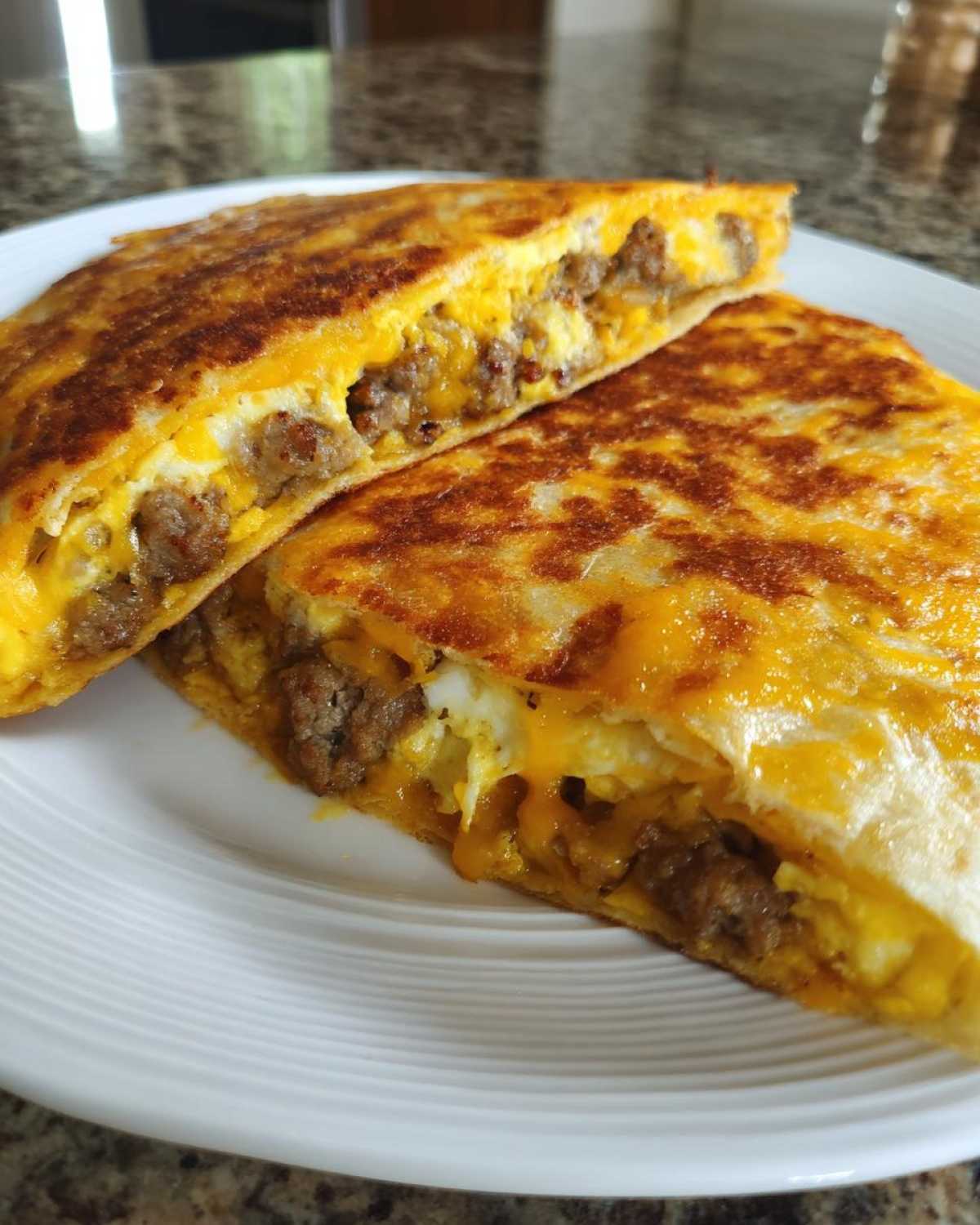 A close-up view of a Sheet Pan Breakfast Quesadillas cut in half, showing melted cheese, scrambled eggs, and sausage filling.
