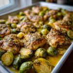 Close-up of juicy Sheet Pan Garlic Butter Chicken and Brussels Sprouts glistening in butter sauce on a baking tray.