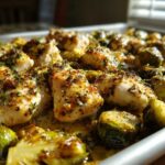 Close-up of juicy Sheet Pan Garlic Butter Chicken and Brussels Sprouts glistening in sauce on a baking tray.