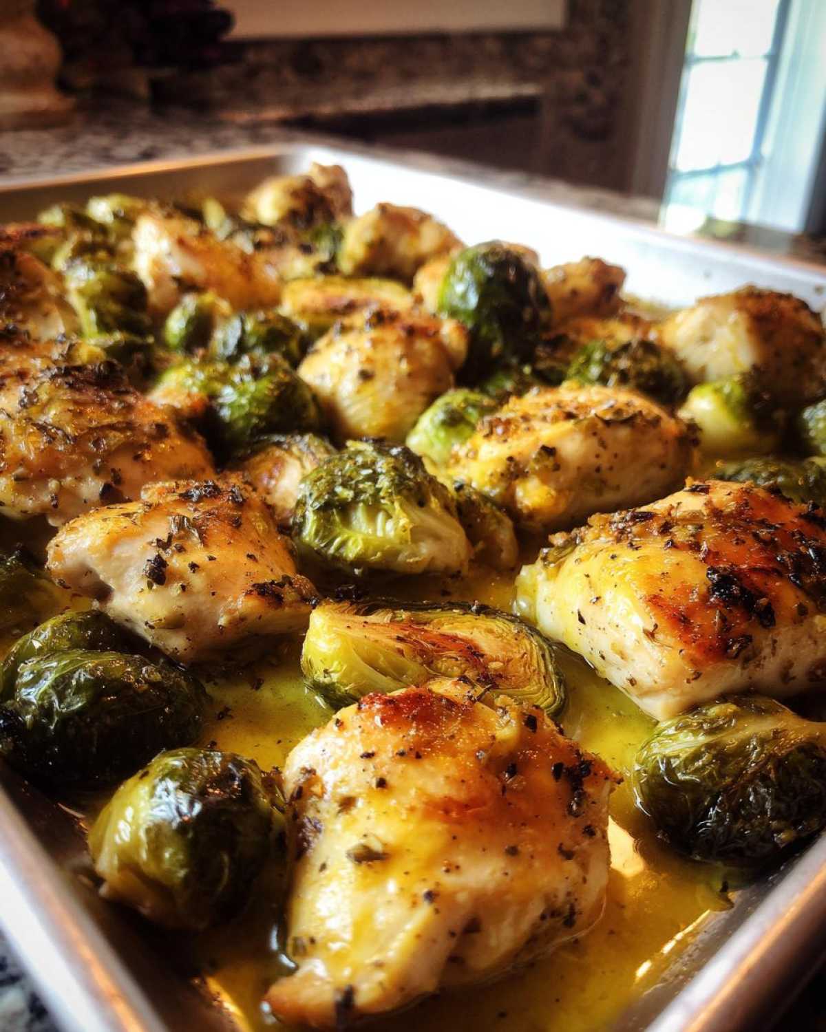 Close-up of cooked Sheet Pan Garlic Butter Chicken and Brussels Sprouts glistening in butter sauce on a baking tray.