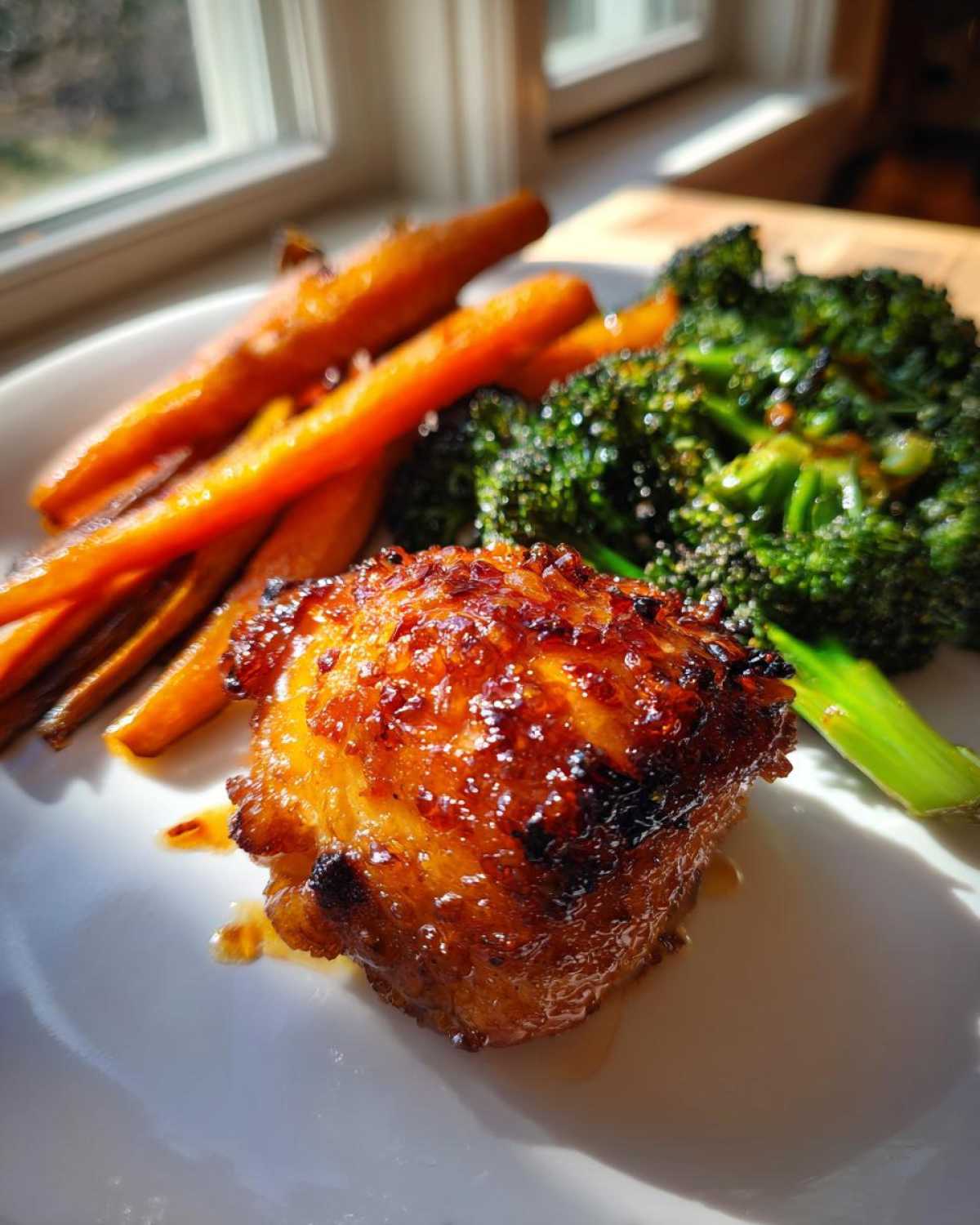 A close-up of a glazed Sheet Pan Ginger Orange Chicken Thighs piece served with roasted carrots and broccoli.