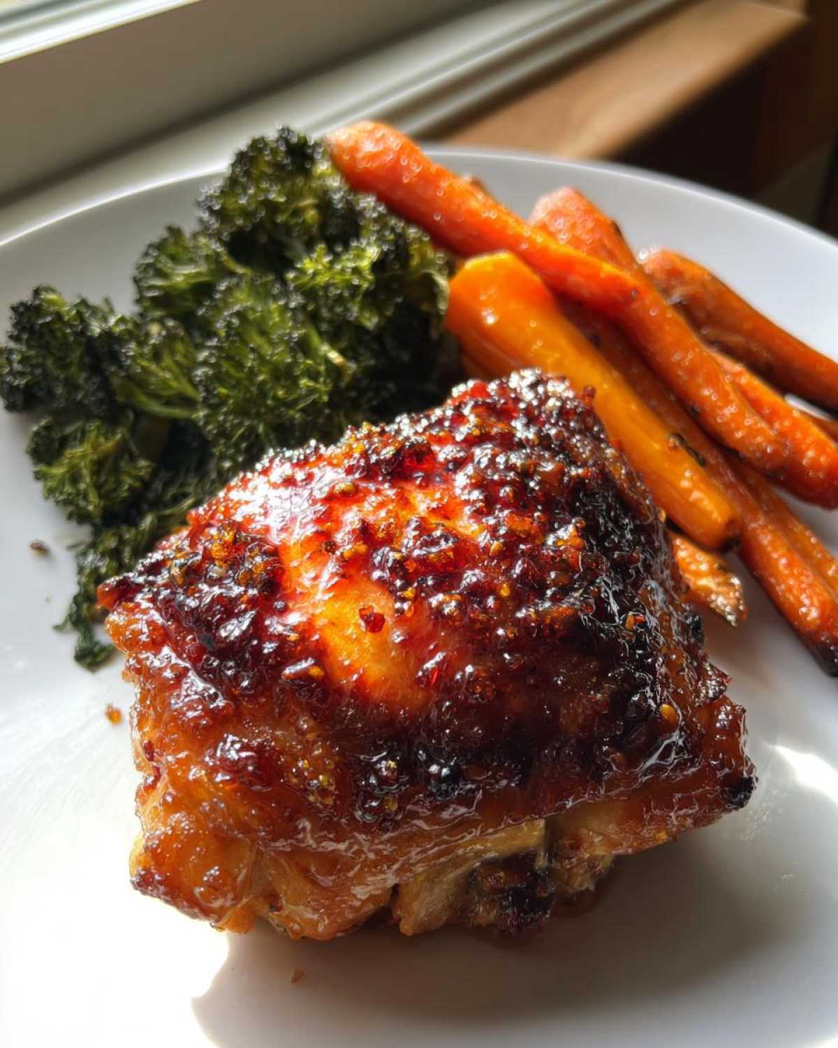 A close-up of a glazed Sheet Pan Ginger Orange Chicken Thighs served with roasted carrots and broccoli.