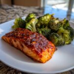 A perfectly cooked fillet of Sheet Pan Honey Harissa Salmon topped with a glossy glaze, served next to roasted broccoli florets.