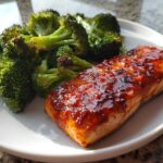 A glistening fillet of Sheet Pan Honey Harissa Salmon served next to bright green roasted broccoli florets on a white plate.
