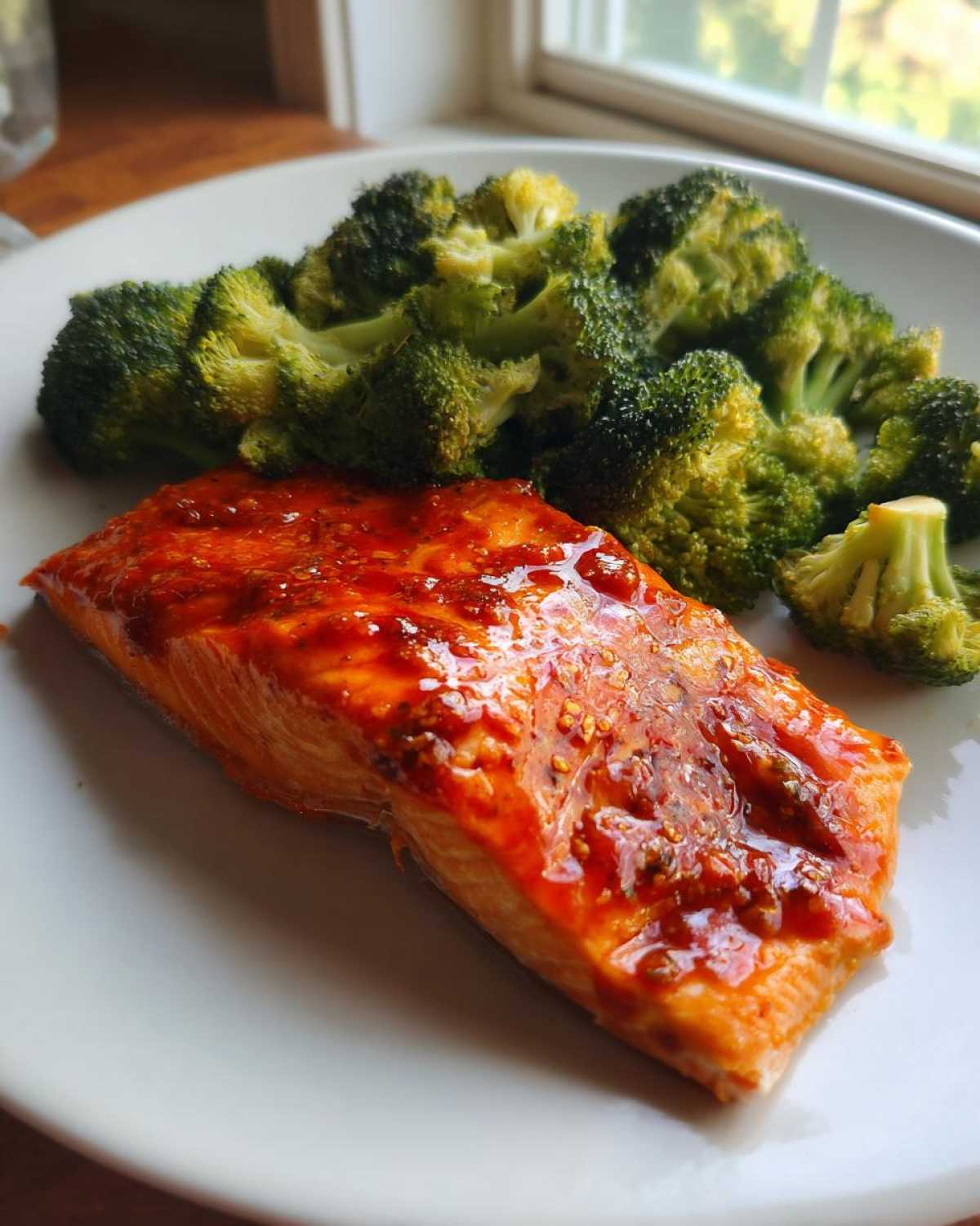 Close-up of a cooked salmon fillet glazed with honey harissa sauce next to bright green broccoli florets.