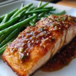 Close-up of a perfectly cooked salmon fillet topped with honey mustard glaze and sesame seeds next to bright green beans.
