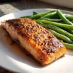 Close-up of a perfectly cooked salmon fillet topped with honey mustard glaze and sesame seeds next to bright green beans.