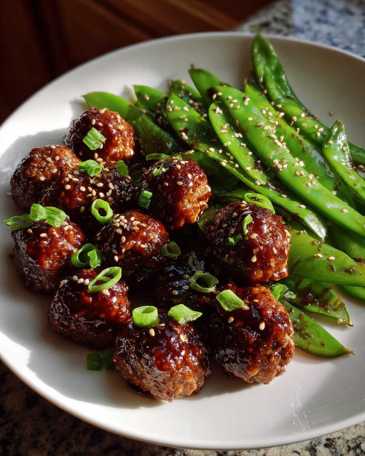Plate of Sheet Pan Sticky Sesame Meatballs glazed in sauce, served with bright green snap peas and sesame seeds.