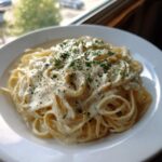 A close-up of spaghetti generously coated in creamy Easy Cottage Cheese Alfredo Sauce, topped with black pepper and parsley.