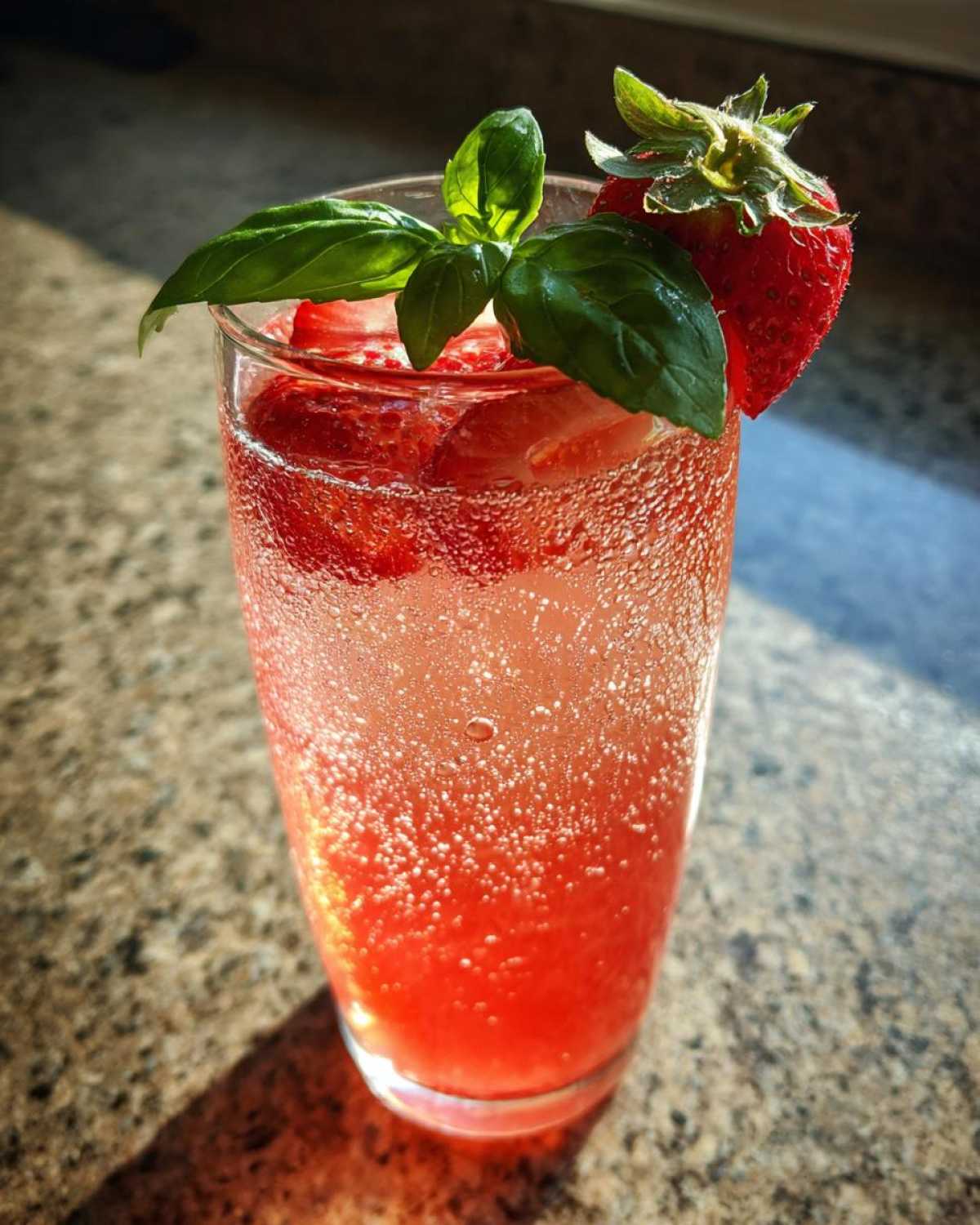 Close-up of a tall glass filled with vibrant Sparkling Strawberry Basil Lemonade, garnished with fresh strawberries and basil.