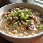 Close-up of a bowl of Vegan Creamy Miso Sesame Noodle Soup topped with mushrooms, scallions, and sesame seeds.