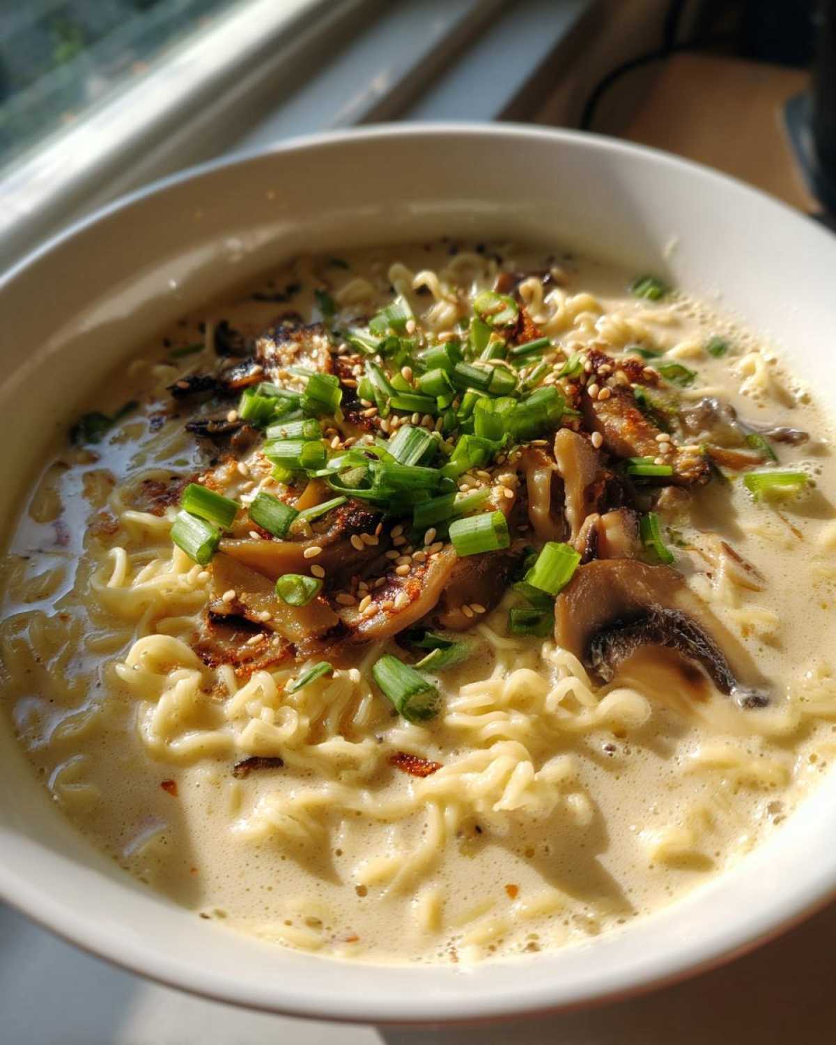 Close-up of Vegan Creamy Miso Sesame Noodle Soup with ramen noodles, mushrooms, and green onions.