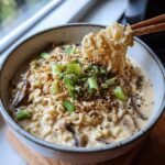 Close-up of Vegan Creamy Miso Sesame Noodle Soup with noodles being lifted by chopsticks, topped with scallions and sesame seeds.