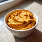 Close-up of thick, bright orange Vegan Creamy Sweet Potato Mac Sauce served in a small white ramekin.