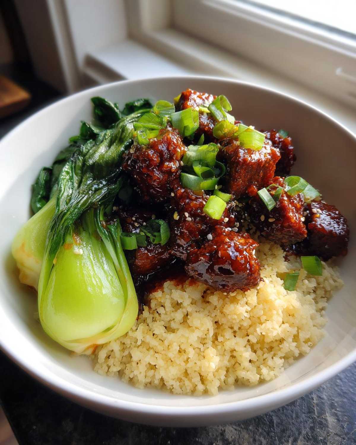 A close-up of a Vegan Crispy Sesame Tempeh Bowl served over couscous with steamed bok choy and green onions.