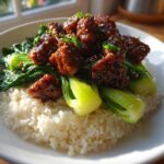 A close-up of a Vegan Crispy Sesame Tempeh Bowl featuring sticky glazed tempeh pieces over white rice and bright green bok choy.