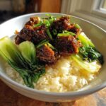 A close-up of a Vegan Crispy Sesame Tempeh Bowl featuring sticky tempeh over white rice and steamed bok choy.
