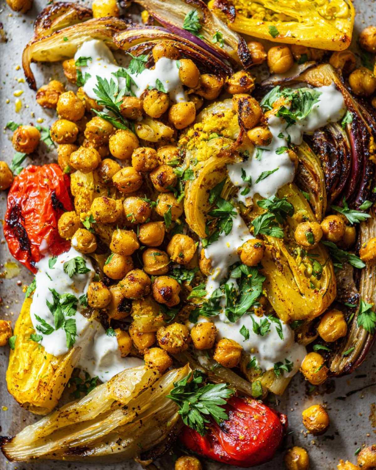 Close-up overhead view of a Vegan One-Pan Chickpea Shawarma Sheet Bake with roasted vegetables, crispy chickpeas, and a white tahini drizzle.