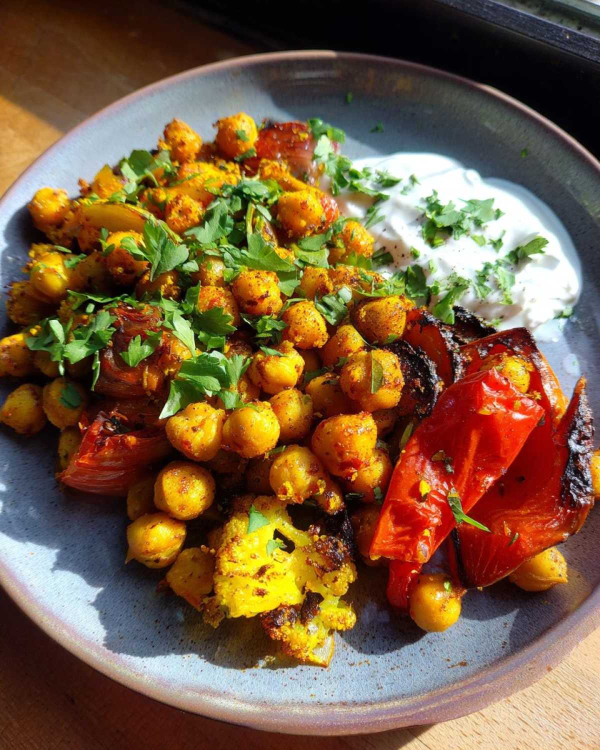 A plate featuring the Vegan One-Pan Chickpea Shawarma Sheet Bake with roasted chickpeas, cauliflower, red pepper, and a dollop of white sauce.