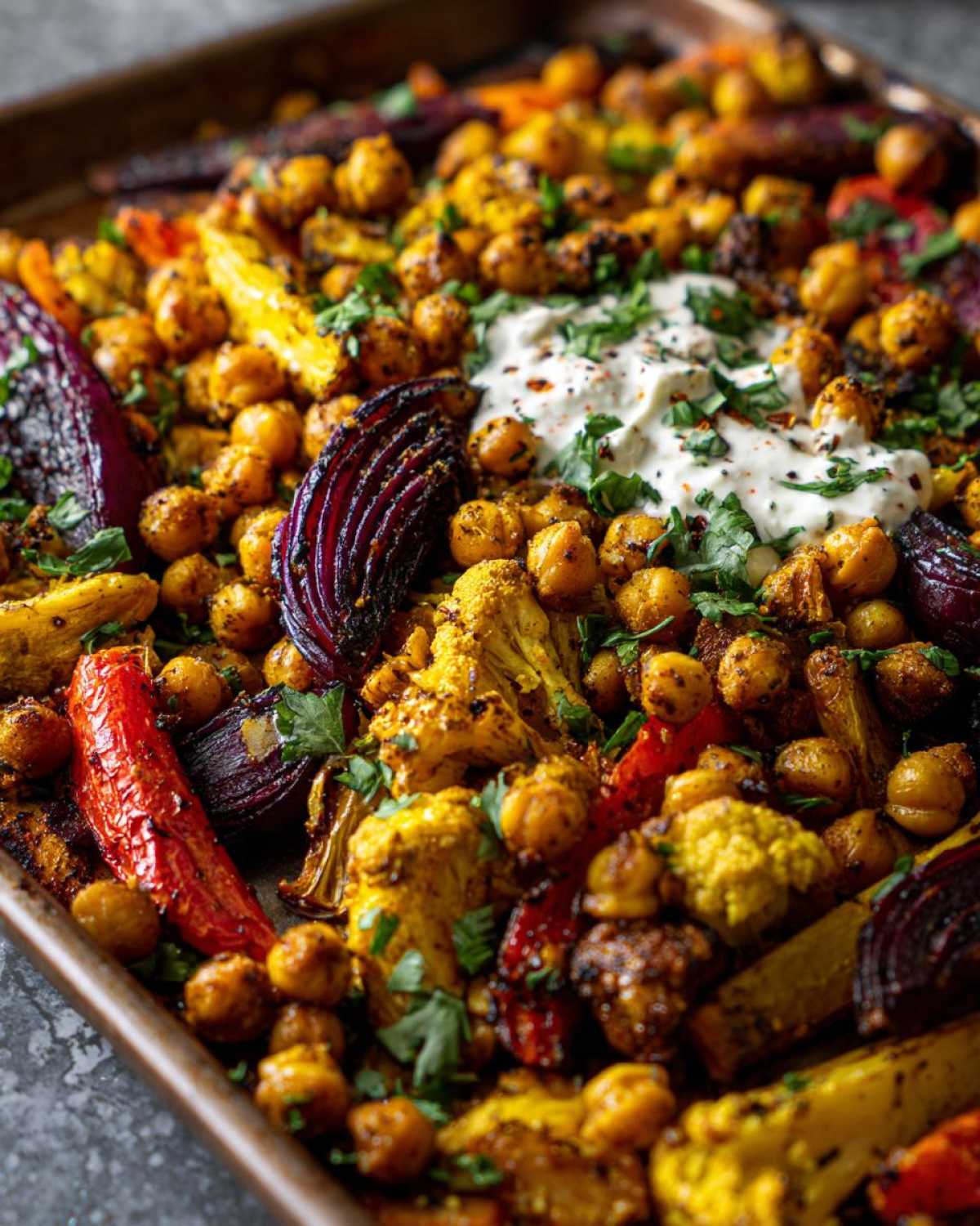 Close-up of the Vegan One-Pan Chickpea Shawarma Sheet Bake featuring roasted chickpeas, colorful vegetables, and a dollop of white sauce.