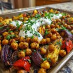 Close-up of a Vegan One-Pan Chickpea Shawarma Sheet Bake with roasted chickpeas, peppers, onions, and a dollop of white sauce.