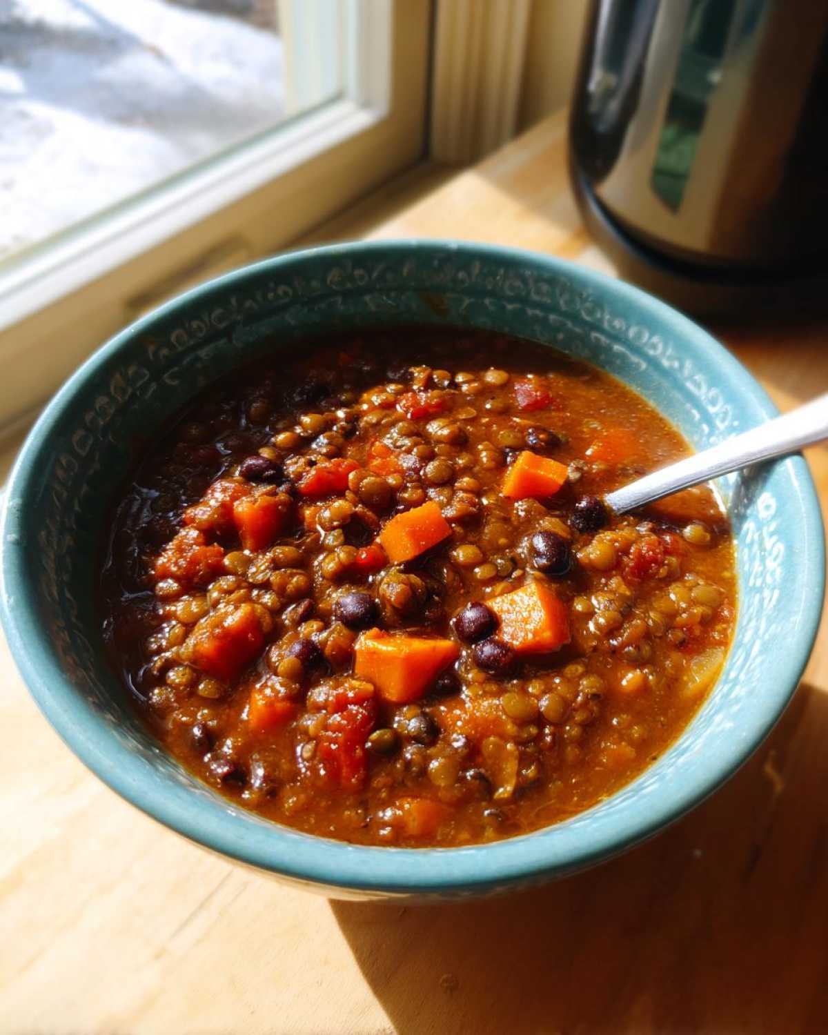 A close-up of a vibrant bowl of Vegan One-Pot Lentil Taco Soup with visible lentils, black beans, and orange sweet potato chunks.