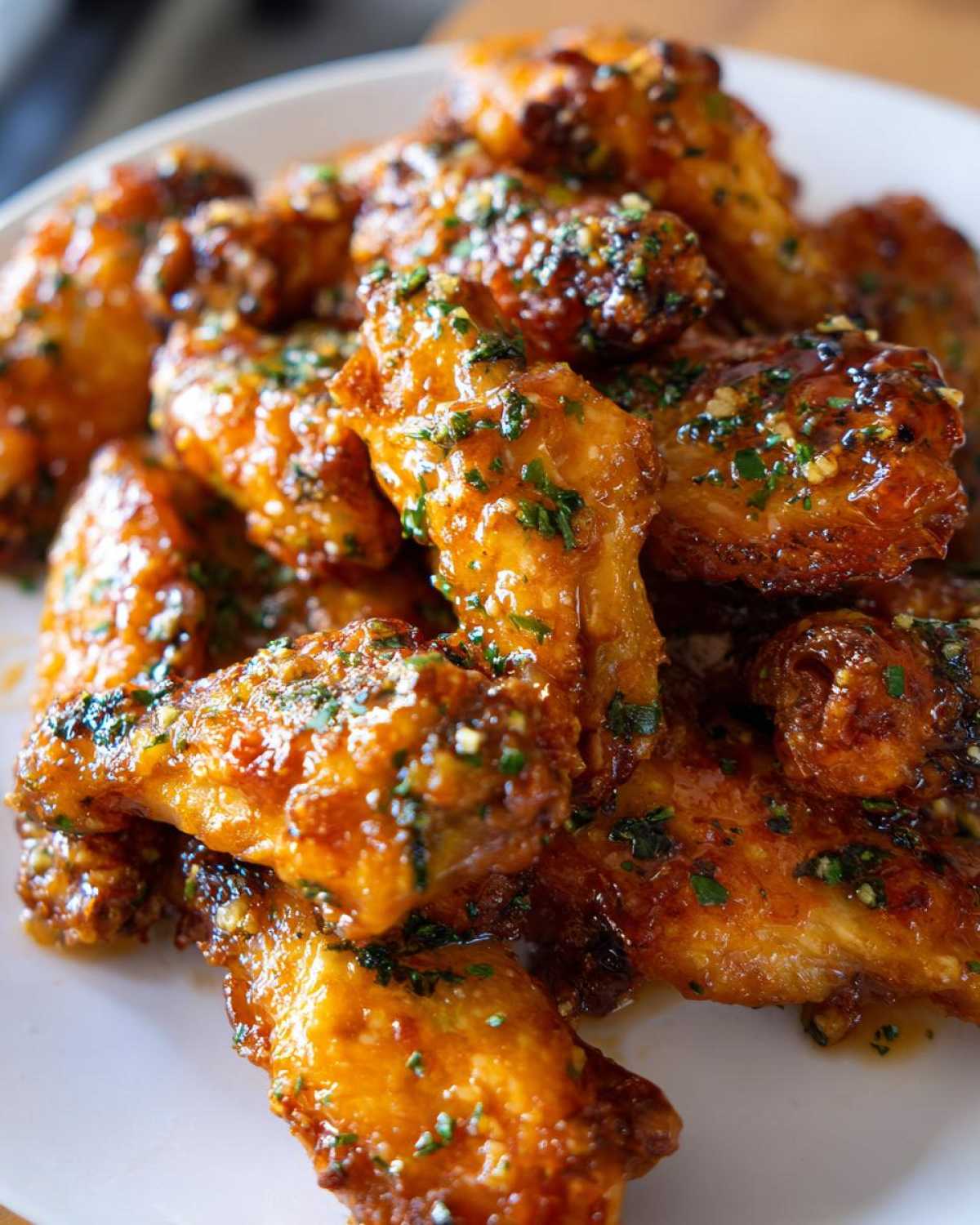 A close-up of crispy chicken wings generously coated in a glossy, savory Copycat Garlic Parmesan Wing Sauce and topped with parsley.