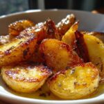 Close-up of perfectly roasted Amazing Greek Lemon Potatoes, glistening with lemon juice and herbs in a white bowl.