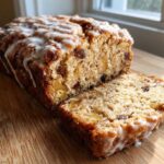 A loaf of Amish Apple Fritter Bread, partially sliced, showing apples and raisins inside, topped with a white glaze.