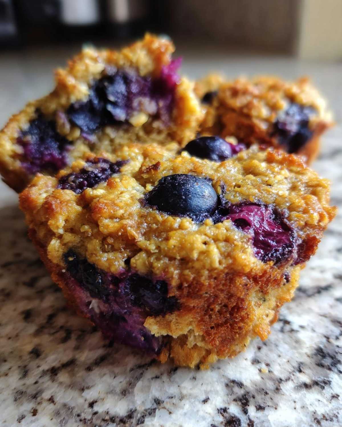 Close-up of a moist, golden-brown Blueberry Oat Muffins No Flour, studded with burst blueberries.