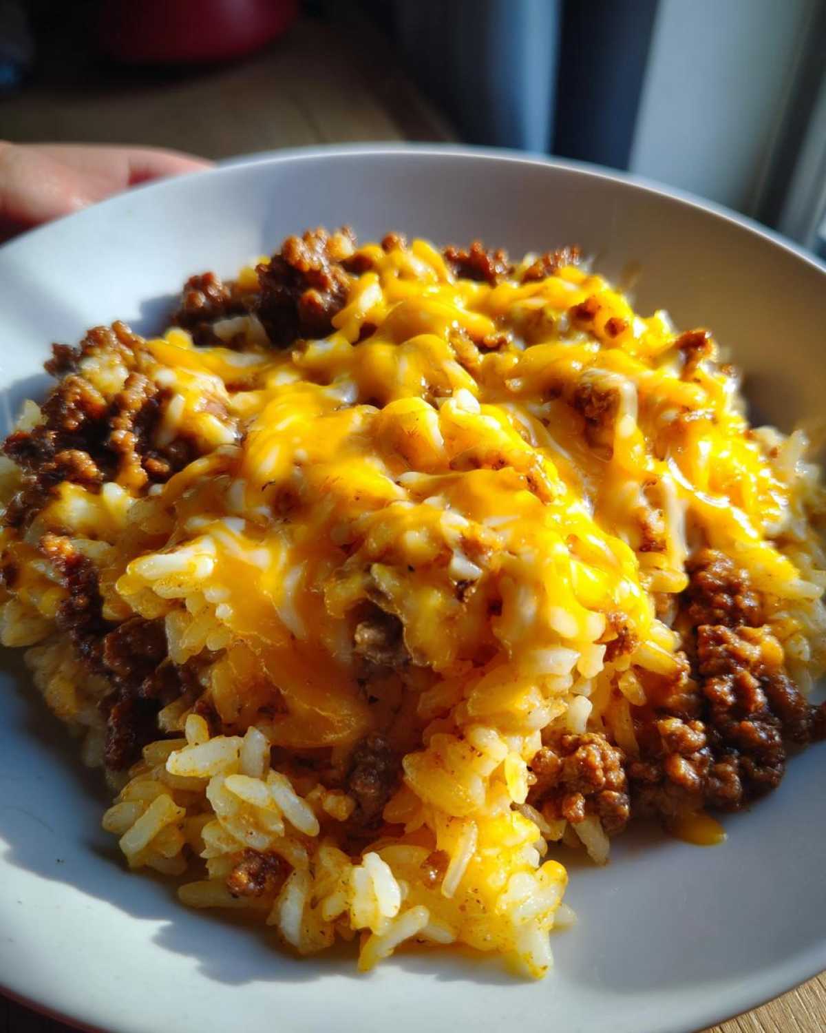 A close-up of a white bowl filled with Cheesy Beef Rice Garlic Butter, topped with melted cheddar cheese.