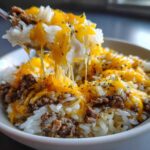 A spoonful of Cheesy Beef Rice Garlic Butter showing melted, stretchy cheddar cheese over rice and ground beef.