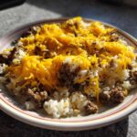 A plate of Cheesy Beef Rice Garlic Butter topped with melted cheddar cheese.