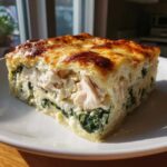 A thick, square slice of Cheesy Chicken Lasagna Spinach showing layers of white chicken, creamy sauce, and green spinach.