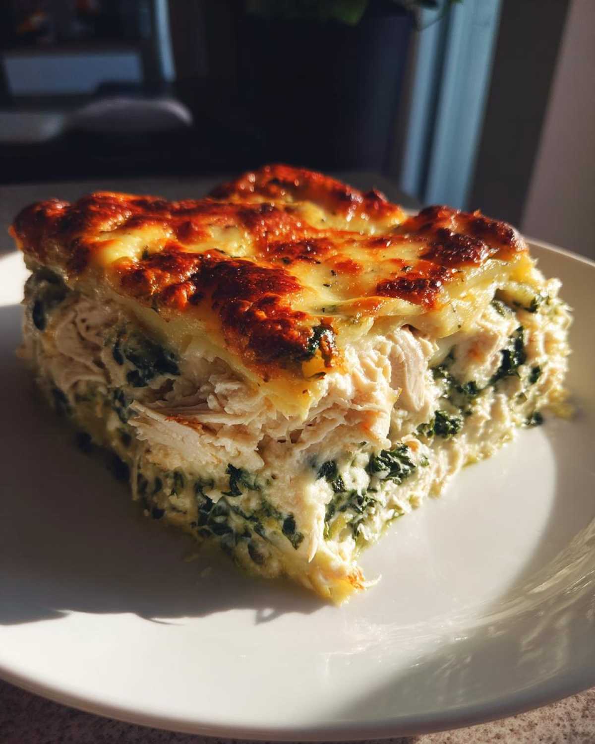 A generous slice of Cheesy Chicken Lasagna Spinach on a white plate, featuring shredded chicken, creamy spinach filling, and a bubbly, browned cheese topping.