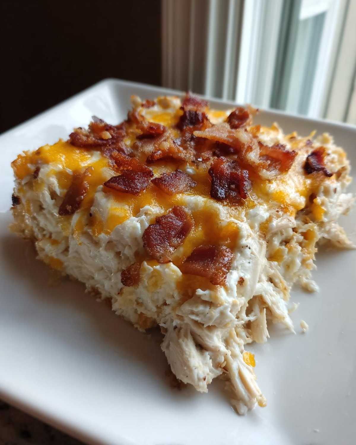 A close-up serving of Cheesy Crack Chicken, featuring shredded chicken, creamy sauce, melted cheddar, and crispy bacon bits.