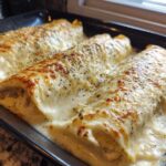 Close-up of three baked Chicken Manicotti Alfredo rolls covered in bubbly, golden-brown cheese sauce.