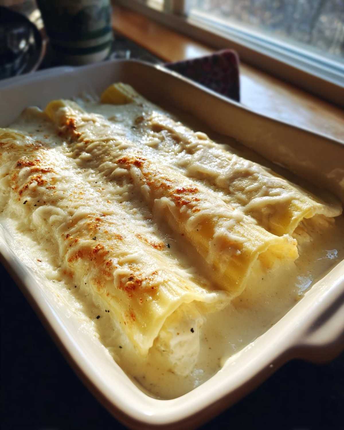 Close-up of baked Chicken Manicotti Alfredo rolls covered in melted cheese and creamy sauce in a baking dish.