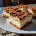 Four squares of rich Churro Cheesecake Bars Dessert with a thick cinnamon-sugar topping, served on a white plate.