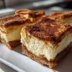 Four square portions of Churro Cheesecake Bars Dessert featuring a thick, creamy filling and a cinnamon-sugar topping on a white plate.