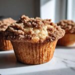 A close-up, low-angle shot of a freshly baked Cinnamon Muffins topped with a thick, sugary cinnamon streusel topping.