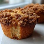 A close-up of a delicious Cinnamon Muffins with a thick, sugary brown streusel topping, showing the texture of the cake base.