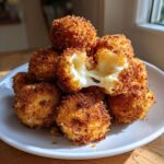 A stack of golden brown Crispy Fried Mozzarella Bites on a white plate, one broken open showing melted, stretching cheese.