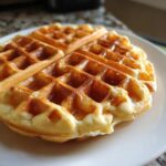 A close-up of a golden brown, fluffy Belgian waffle drizzled with syrup, ready to eat.