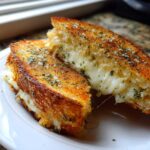 Close-up of a perfectly grilled Garlic Bread Grilled Cheese sandwich cut in half, showing gooey melted cheese and herbs.