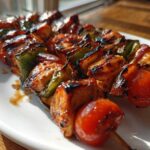 Two skewers of perfectly grilled and glazed Chicken Kabobs featuring charred chicken, green peppers, and cherry tomatoes on a white plate.