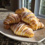 A plate piled high with golden brown Cinnamon Roll Crescents drizzled with white icing.