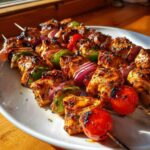 Close-up of perfectly grilled Chicken Kabobs featuring marinated chicken, red onion, green pepper, and cherry tomatoes on skewers.