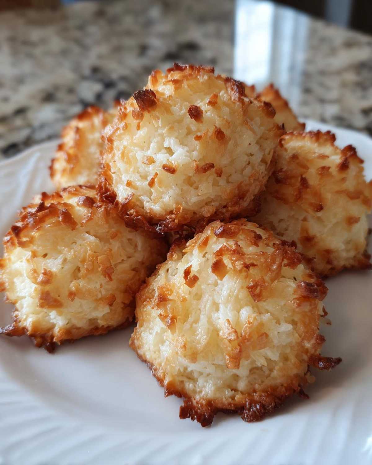 A close-up of several golden brown Low Carb Coconut Cookies stacked on a white plate.