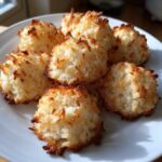 A close-up of several perfectly baked, golden-edged Low Carb Coconut Cookies piled on a white plate.
